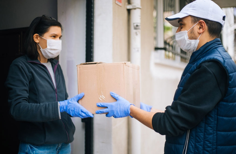 Courier in protective mask delivers parcel to client